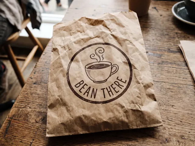 Crumpled paper bag with a round coffee shop logo on a café table, original photo