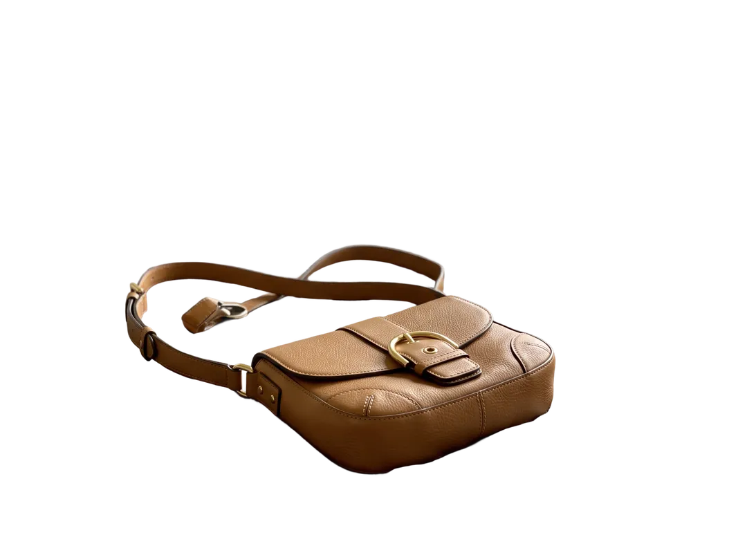 Tan leather crossbody bag on an unmade bed, background removed (transparent PNG)