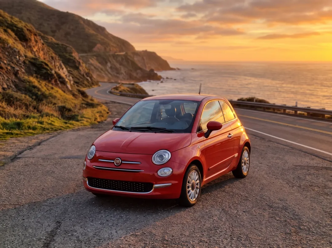 Red hatchback with the background changed to coastal highway at sunset