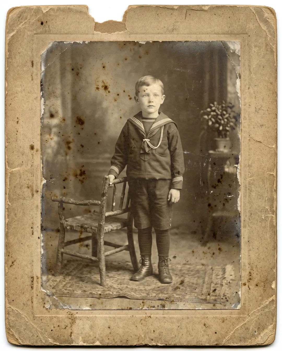 Damaged old photo of a 1910s cabinet-card portrait of a boy in a sailor suit: extreme fading, a chipped top edge