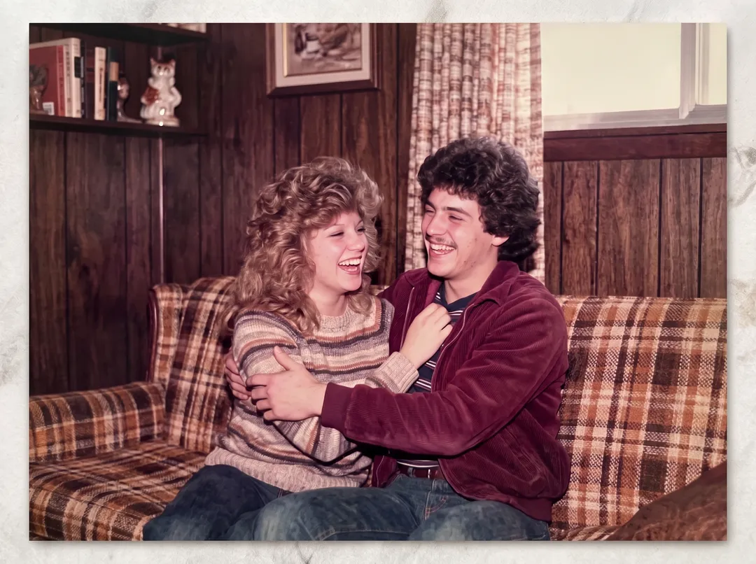 Restored photo of a 1980s couple laughing on a plaid sofa
