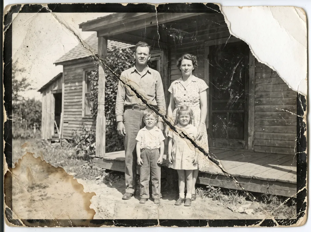 Damaged old photo of a 1950s family of four in front of a farmhouse porch: diagonal crease, cracks, scratches, water stain