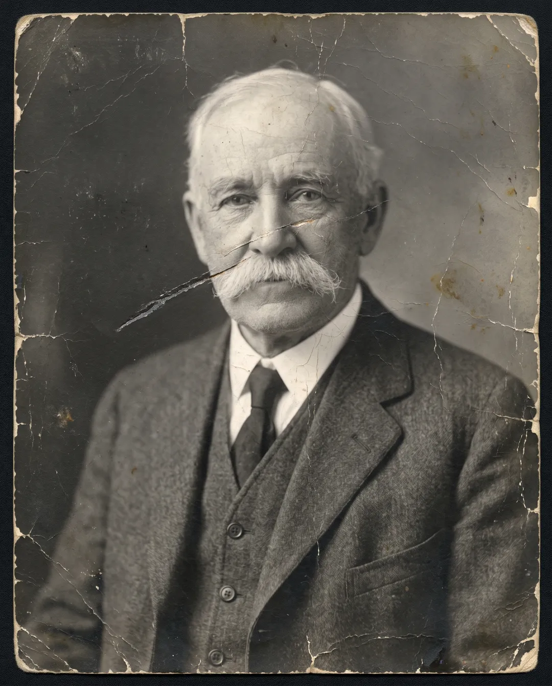 Damaged old photo of a 1930s studio portrait of an elderly man with a white mustache: blur, heavy grain, a scratch across the face
