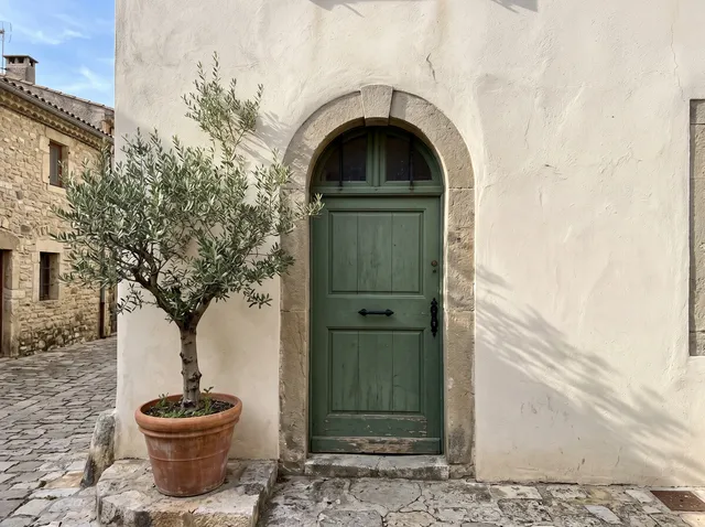 Cream stucco wall with a green door and olive tree, after removing the graffiti