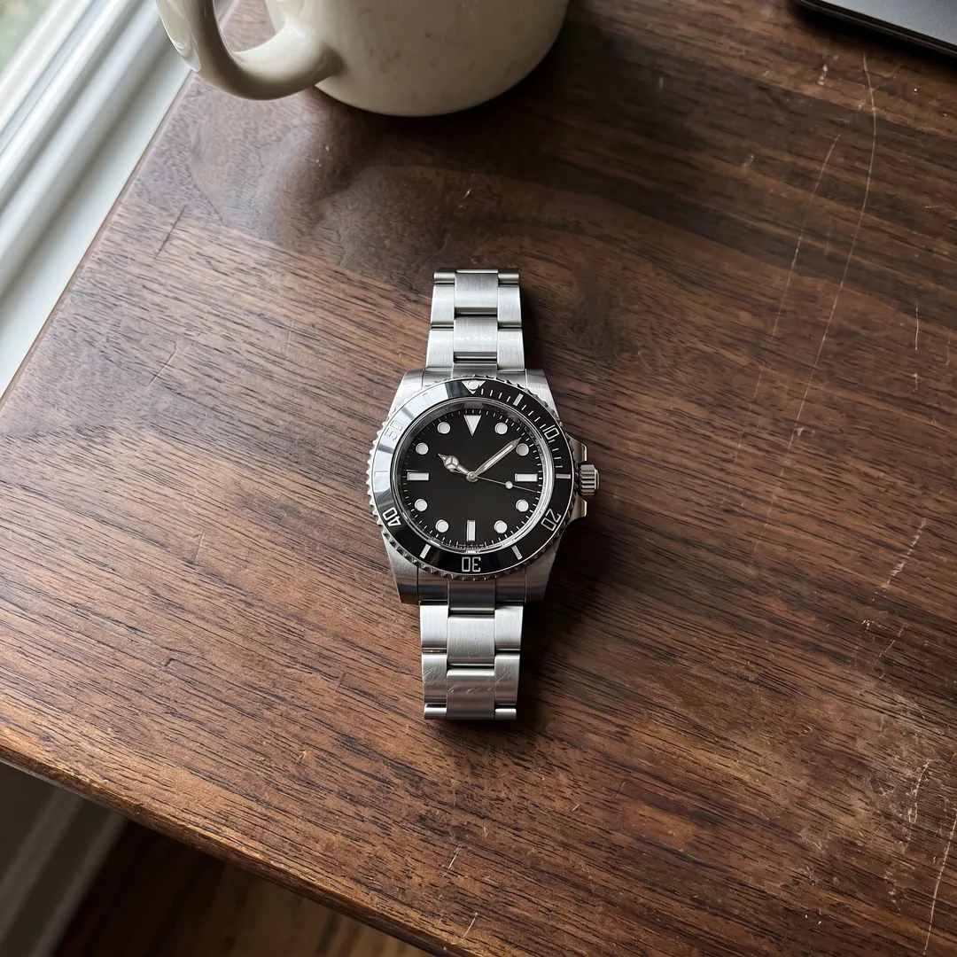 Silver dive watch on a walnut desk, after removing the sticky note, paperclip and coffee stain
